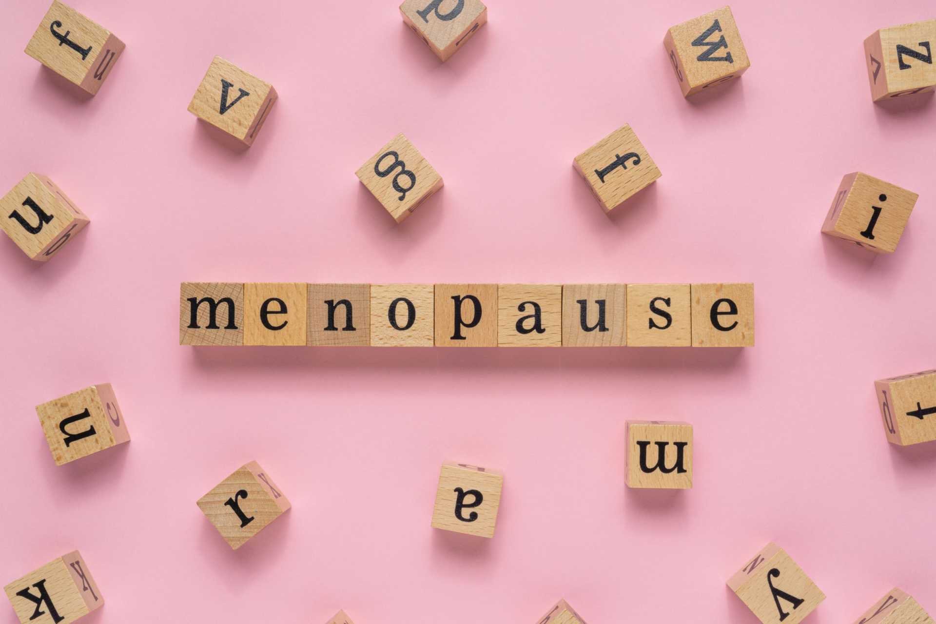 Scrabble tiles spelling out menopause on a pink background