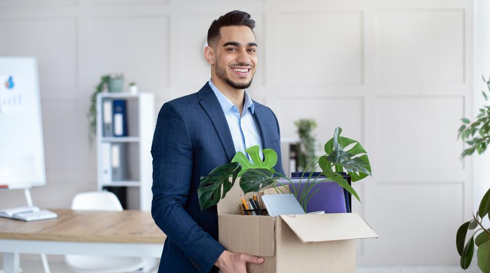 A young man carrying a box with a plant in it as he starts his new job